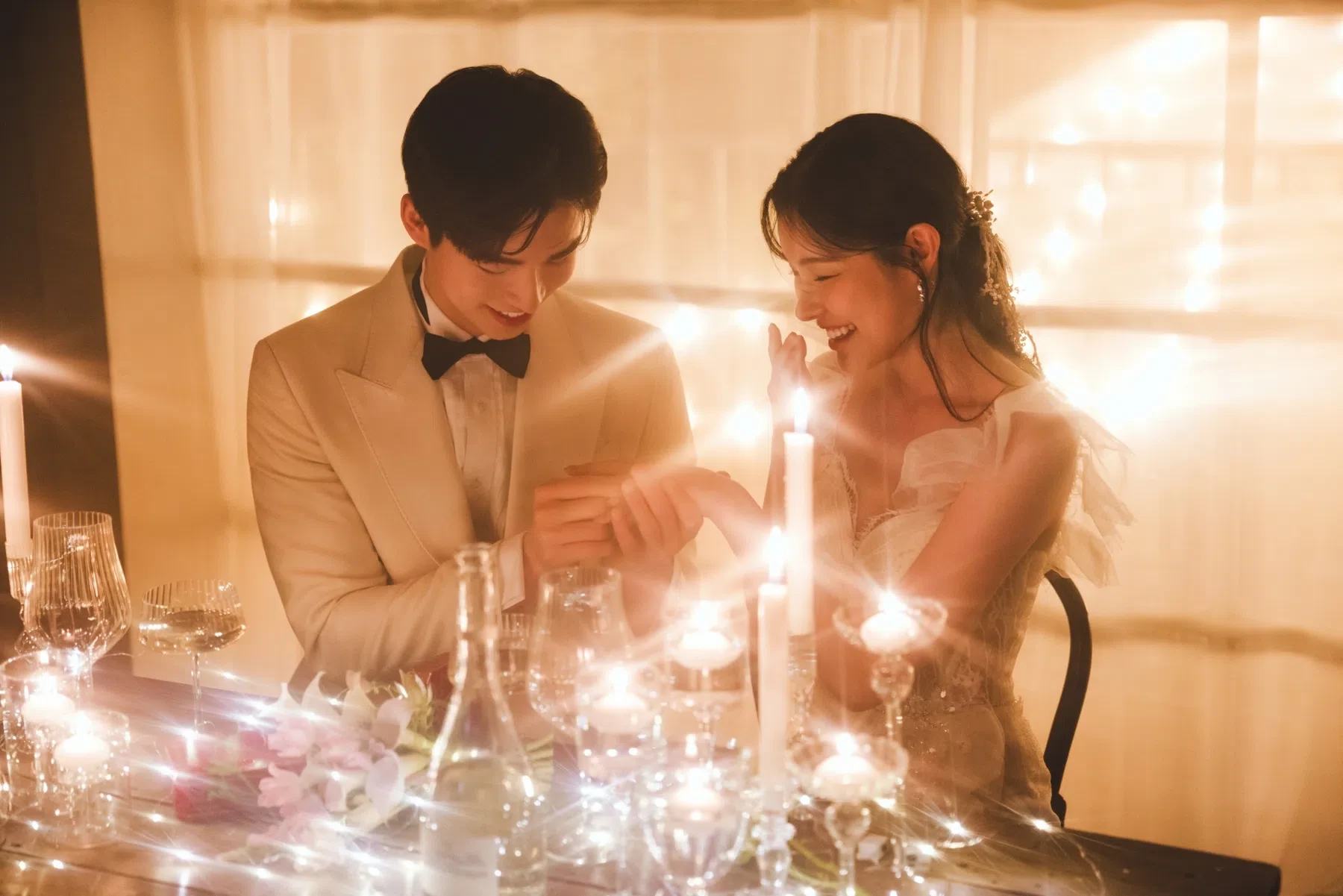 촛불이 놓인 실내 테이블의 자연광과 여백을 살린 커플 클로즈업입니다. 의상 실루엣과 표정 중심의 깨끗한 무드를 확인하기 좋습니다.