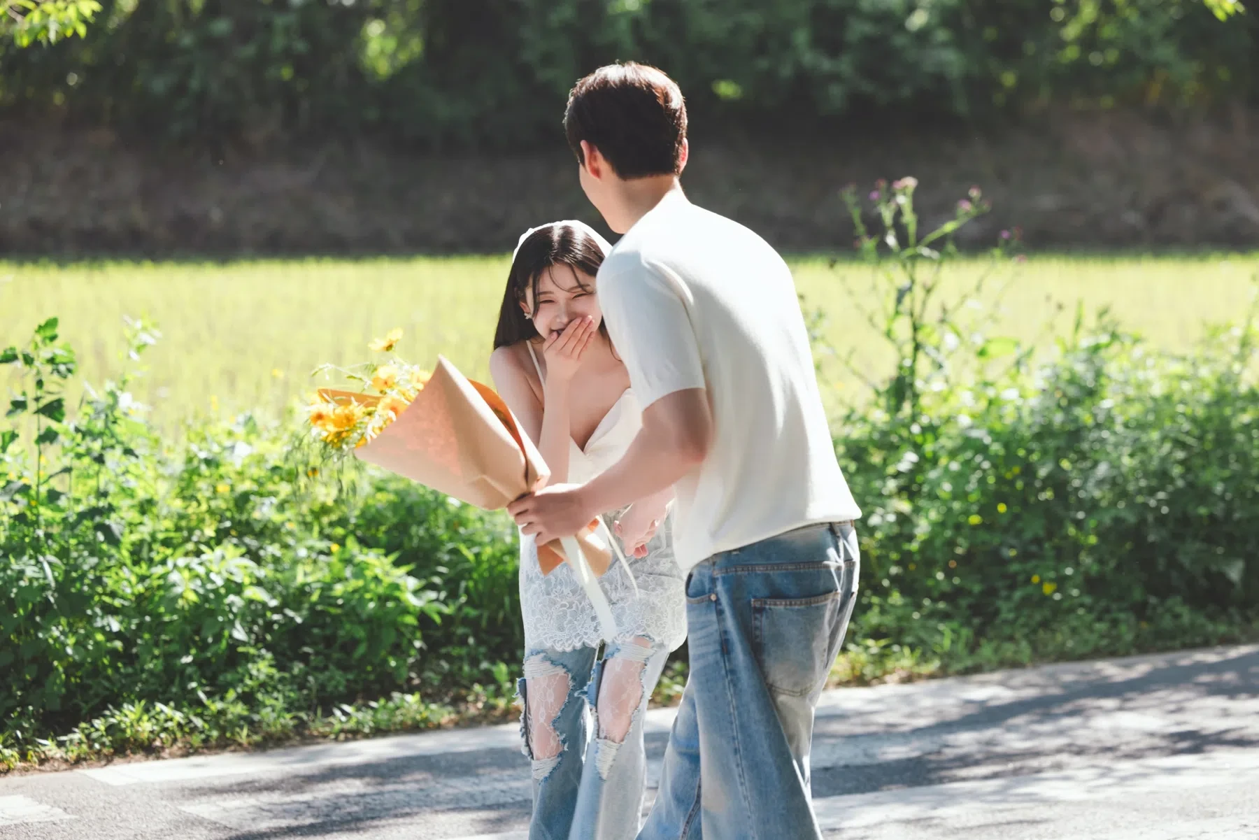 나무가 이어진 도로의 계절감과 동선을 살린 야외 스토리 컷입니다. 자연스러운 움직임과 초록 배경을 원하는 커플에게 어울립니다.