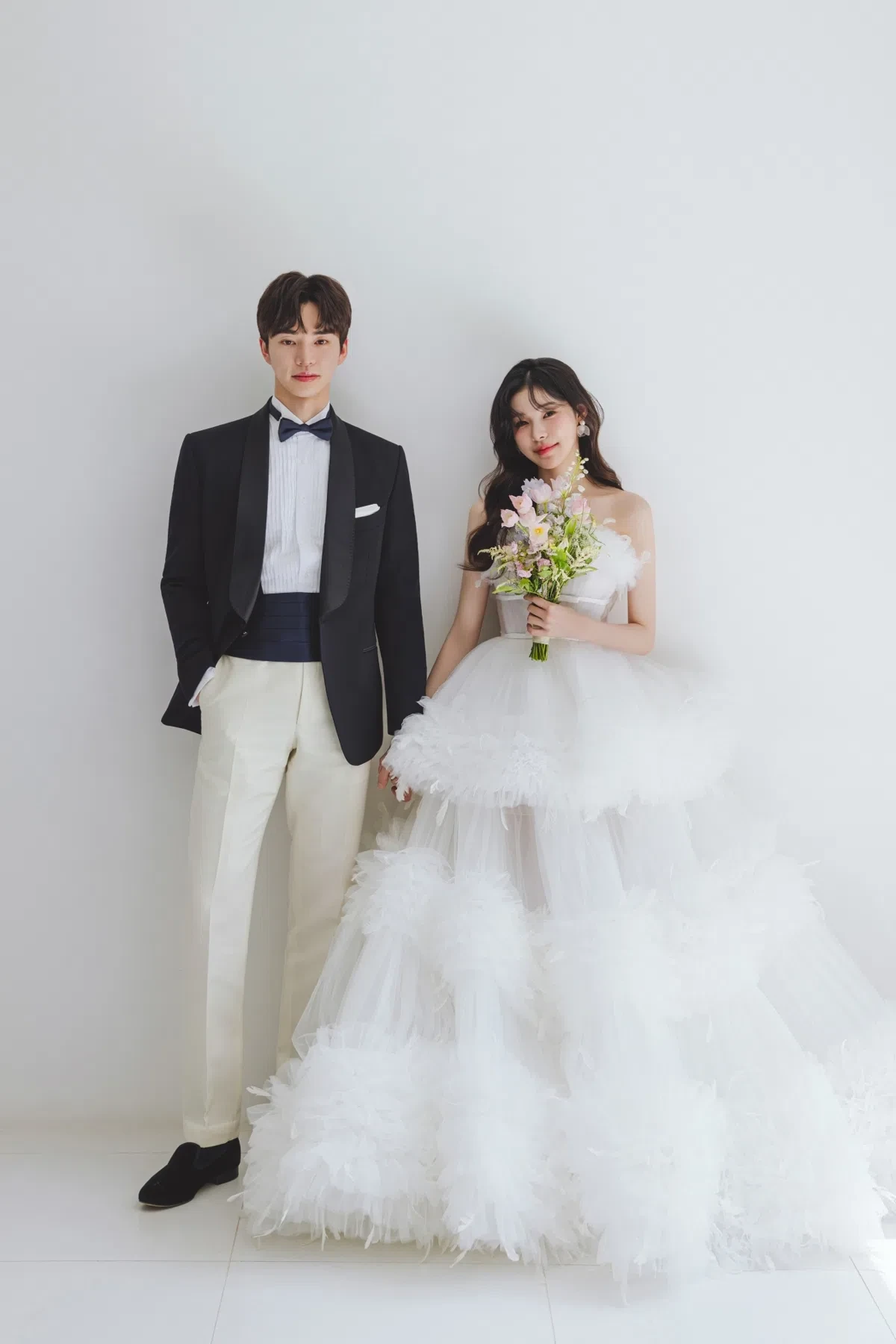 화이트 스튜디오의 자연광과 여백을 살린 포멀 커플 컷입니다. 의상 실루엣과 표정 중심의 깨끗한 무드를 확인하기 좋습니다.