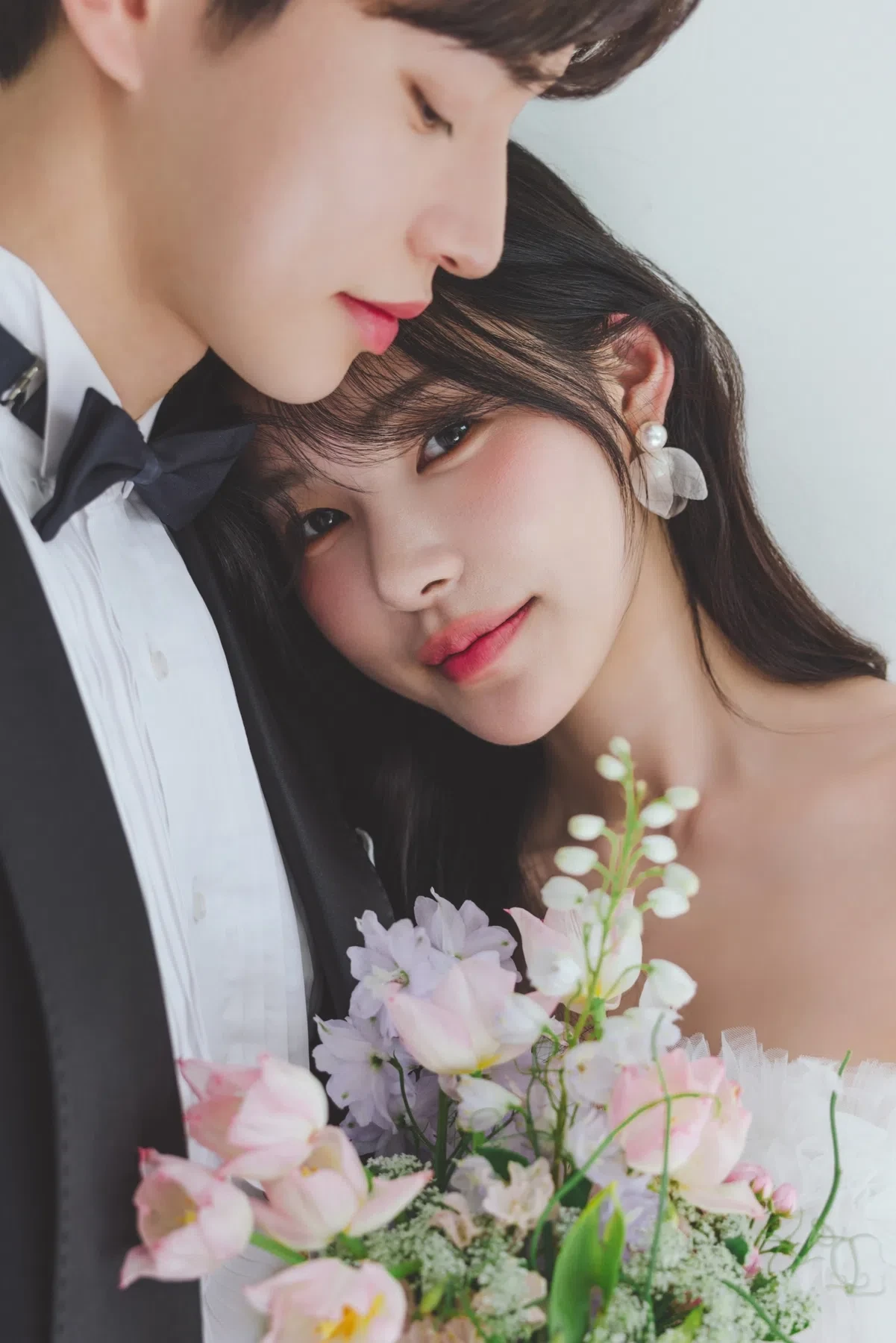 화이트 스튜디오의 자연광과 여백을 살린 커플 클로즈업입니다. 의상 실루엣과 표정 중심의 깨끗한 무드를 확인하기 좋습니다.