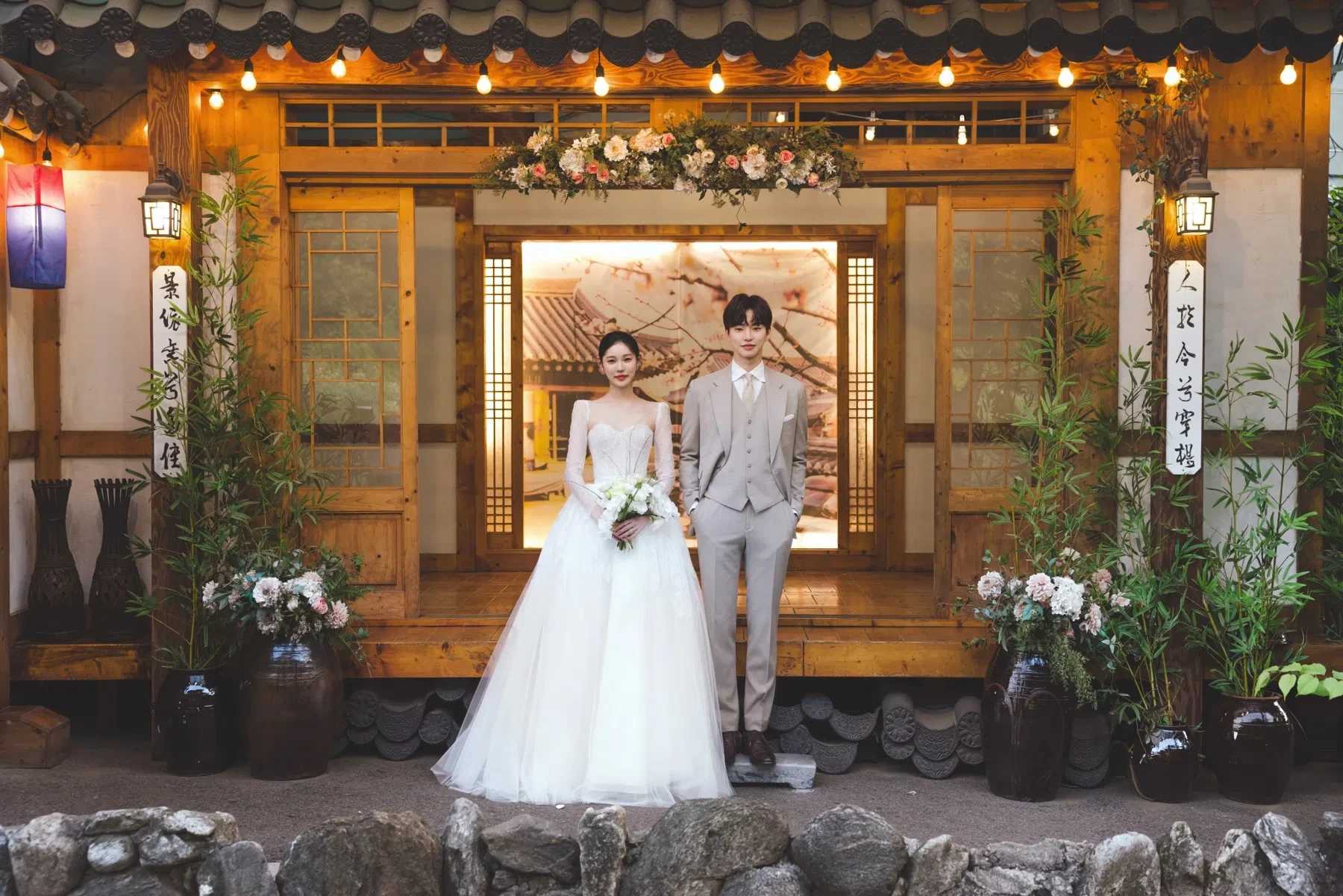 hanok exterior의 계절감과 동선을 살린 포멀 커플 컷입니다. 자연스러운 움직임과 초록 배경을 원하는 커플에게 어울립니다.