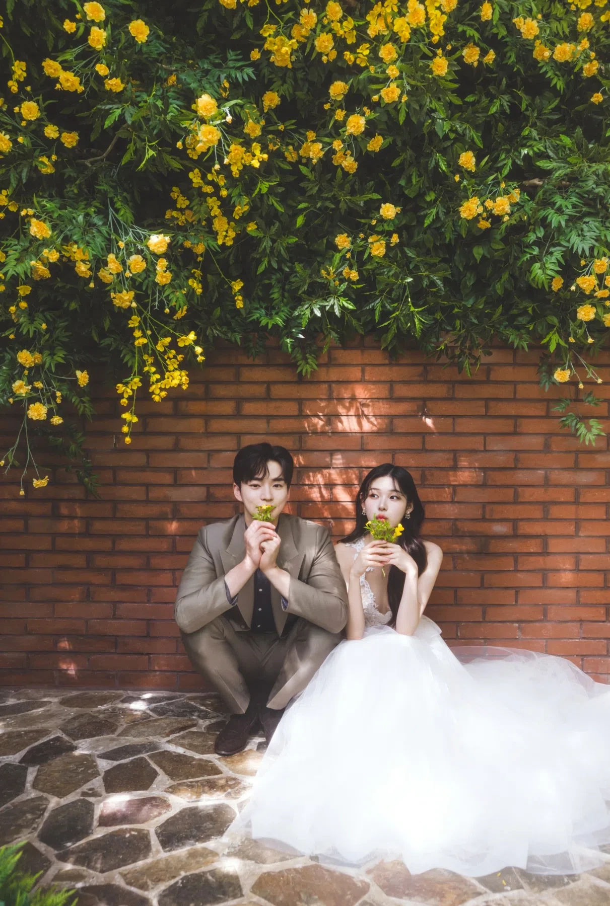 벽돌 플라워 월의 계절감과 동선을 살린 라이프스타일 커플 컷입니다. 자연스러운 움직임과 초록 배경을 원하는 커플에게 어울립니다.