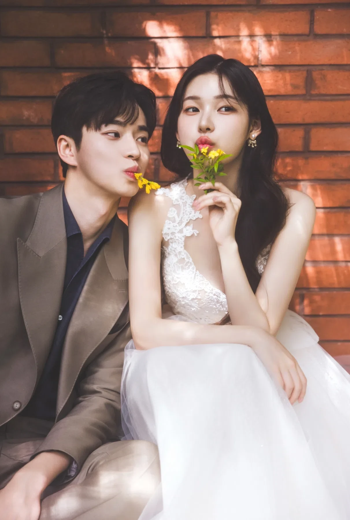 벽돌 플라워 월의 계절감과 동선을 살린 커플 클로즈업입니다. 자연스러운 움직임과 초록 배경을 원하는 커플에게 어울립니다.