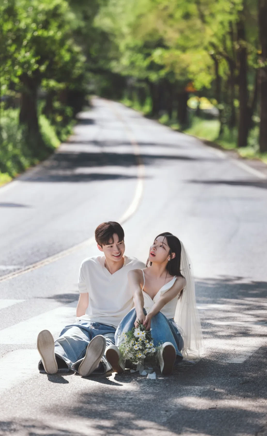 숲길 도로의 계절감과 동선을 살린 라이프스타일 커플 컷입니다. 자연스러운 움직임과 초록 배경을 원하는 커플에게 어울립니다.