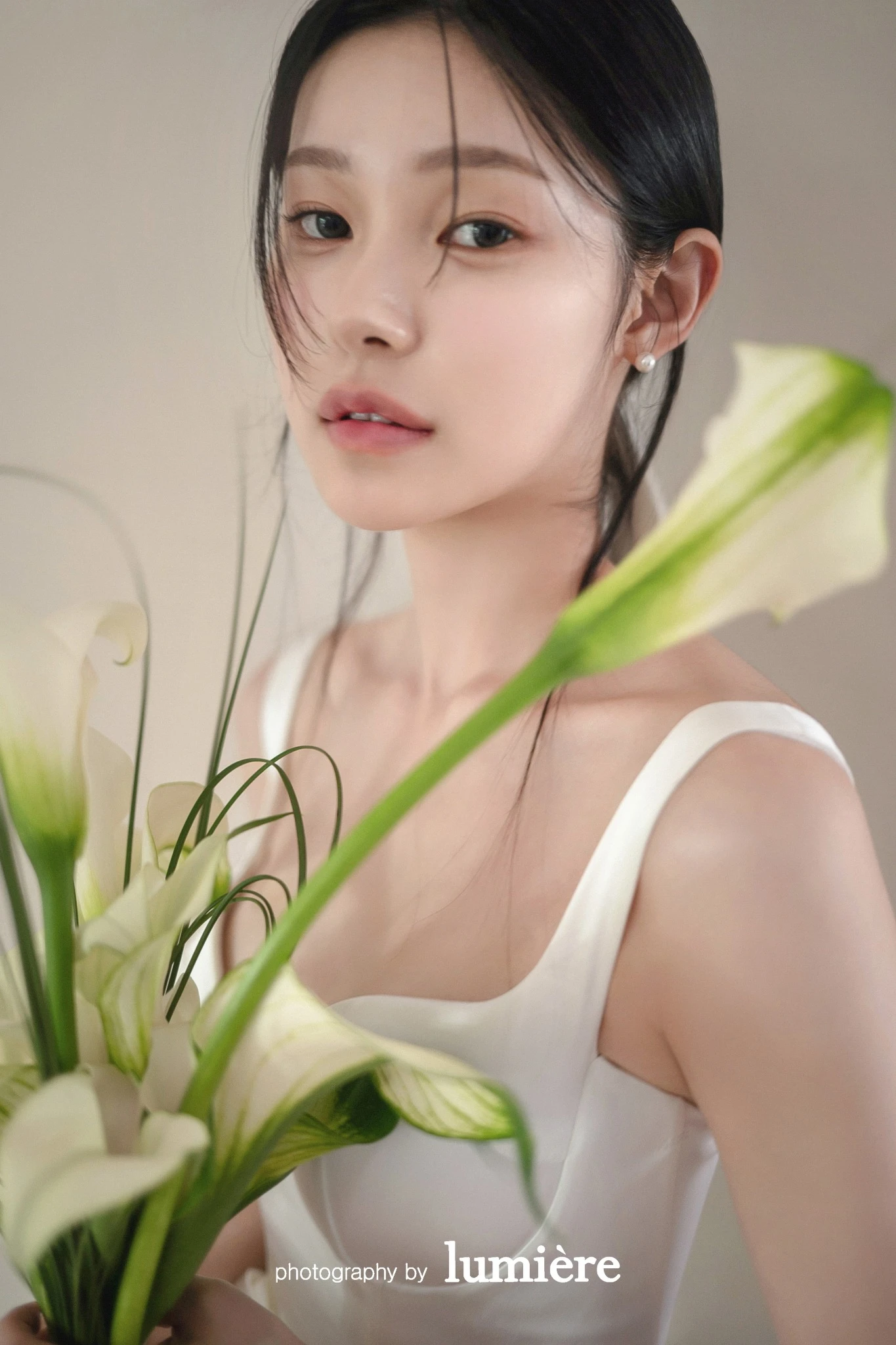 베이지 실내 세트와 칼라꽃 가까이에서 화이트 의상의 여성 단독이 칼라꽃 앞에서 얼굴을 가까이 보임 모습이다. 칼라꽃·화이트 의상이 함께 보인다.