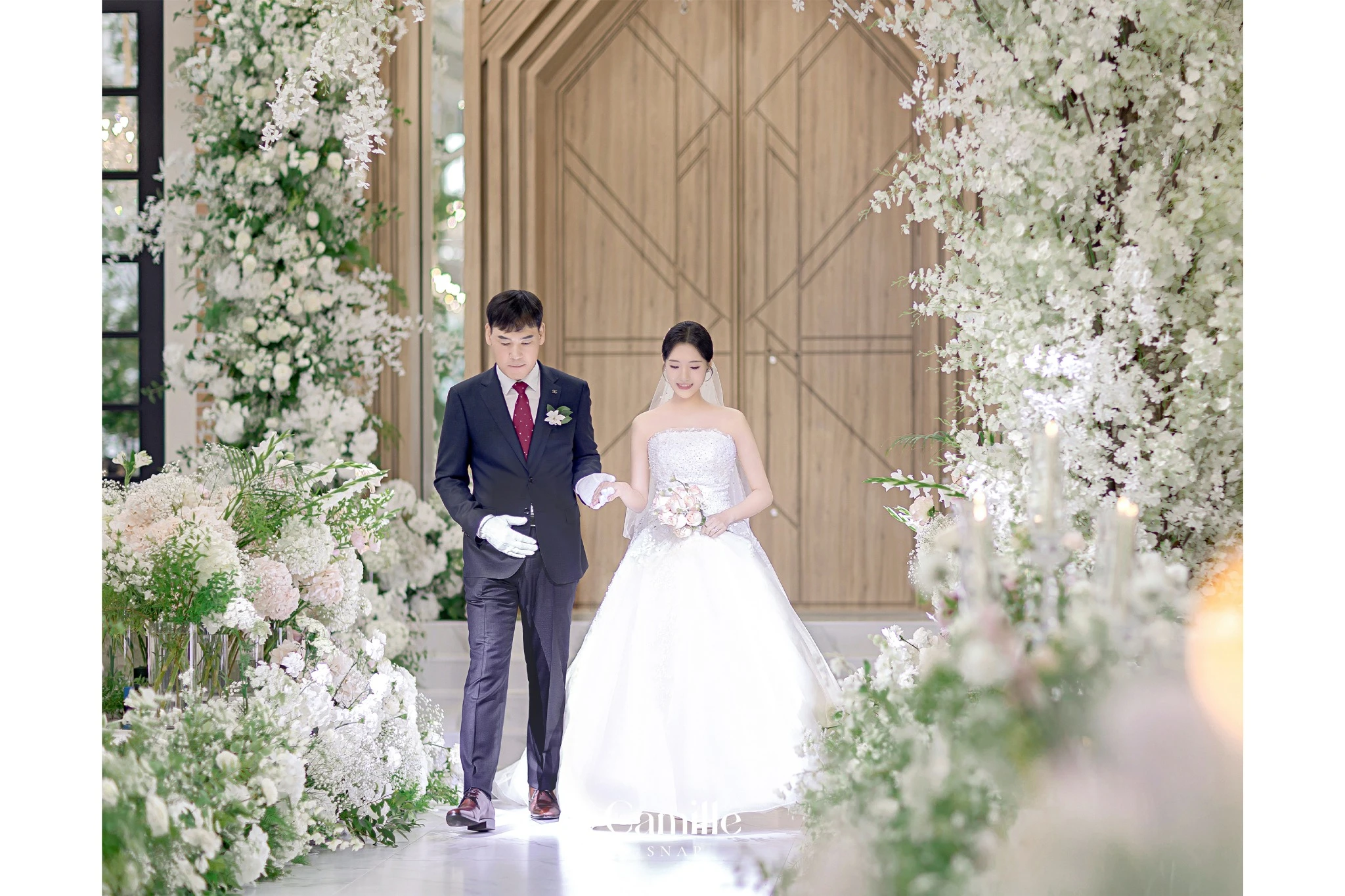예식 공간의 플라워 장식 사이로 신부가 입장하는 장면입니다.