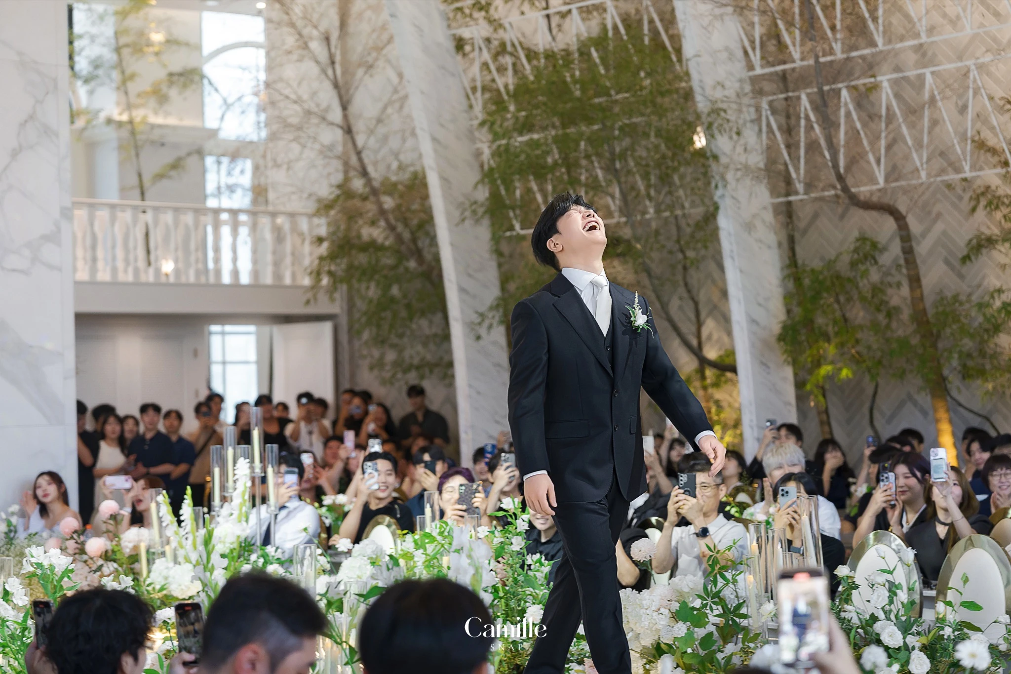 하객들의 시선 속에서 신랑의 밝은 표정이 담긴 현장 컷입니다.