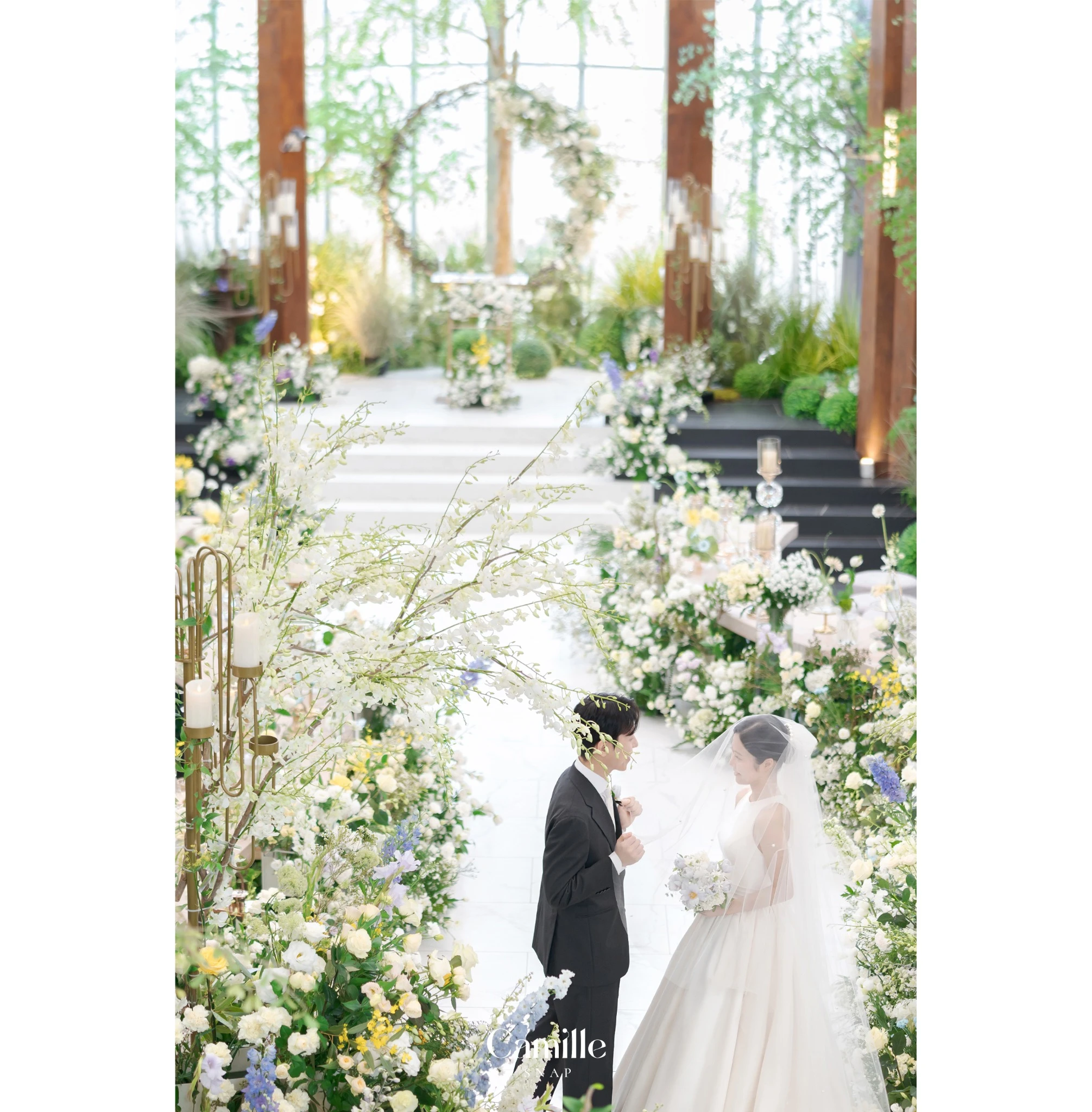 예식 공간의 플라워 장식 사이에 선 신랑신부의 본식 컷입니다.