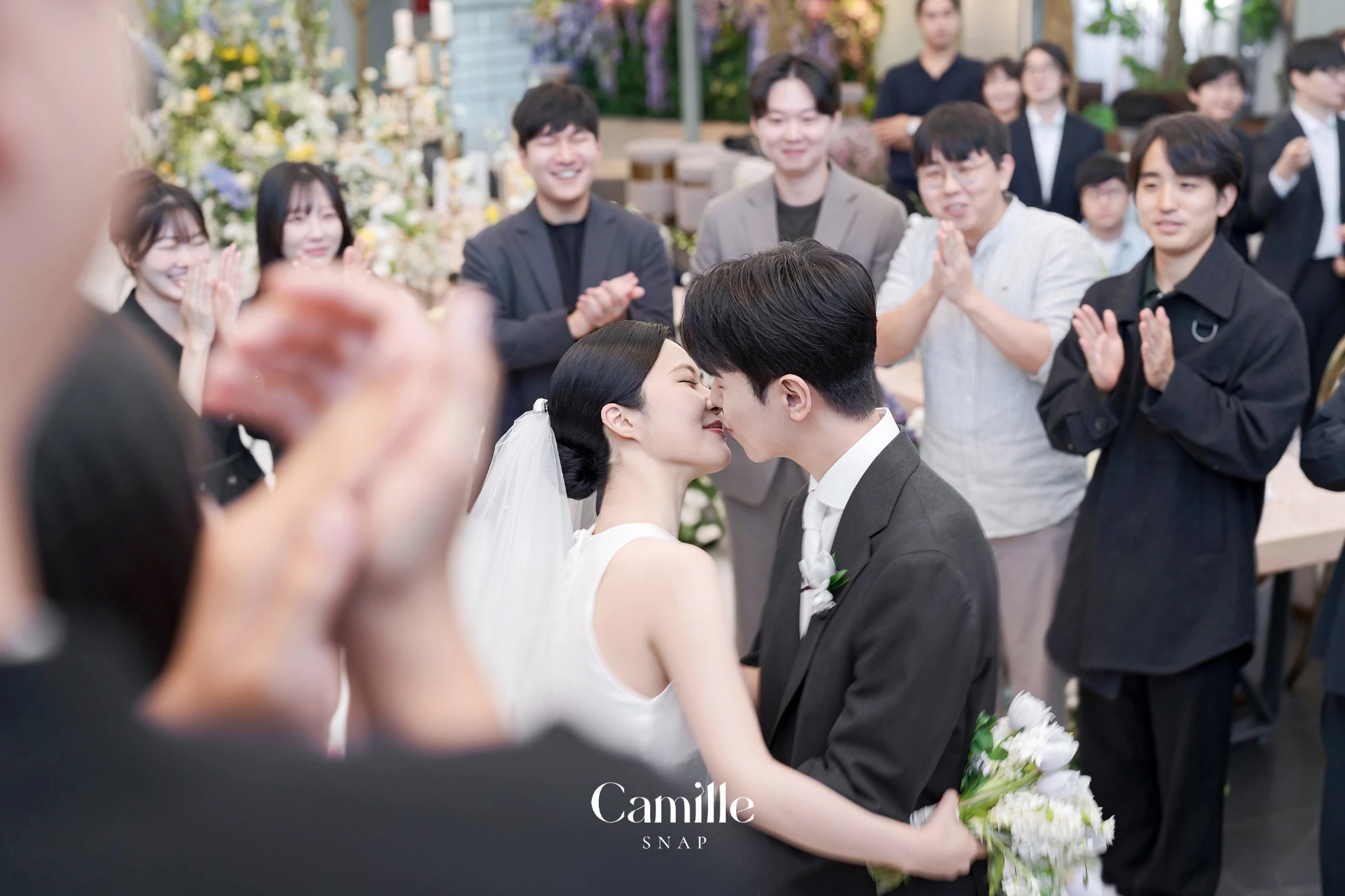 하객의 축하와 신랑신부의 본식 순간이 함께 담긴 컷입니다.