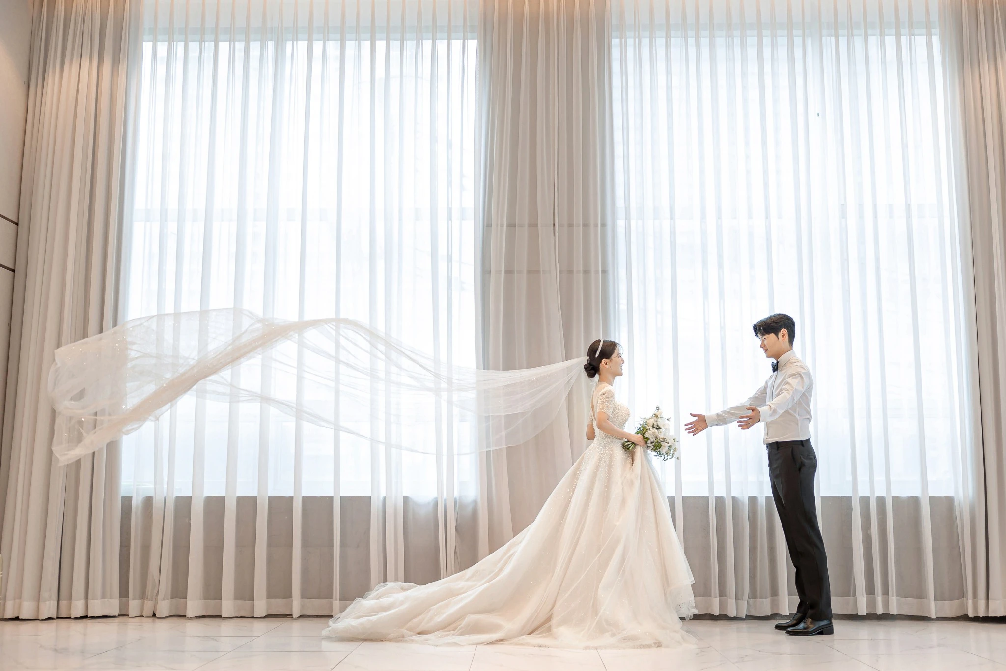 연회장 전경 커플 컷으로, 넓은 연회장과 플라워 테이블 장식와 샹들리에과 하객석가 함께 보이는 장면입니다.
