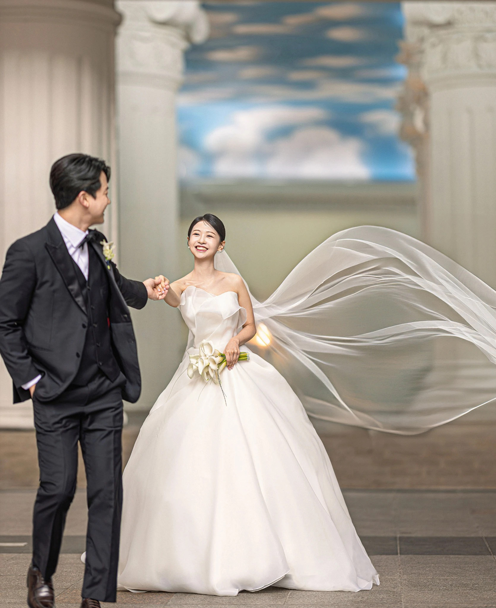베일 연출 커플 컷으로, 기둥과 천장 그림이 보이는 실내 로비와 긴 베일와 기둥가 함께 보이는 장면입니다.