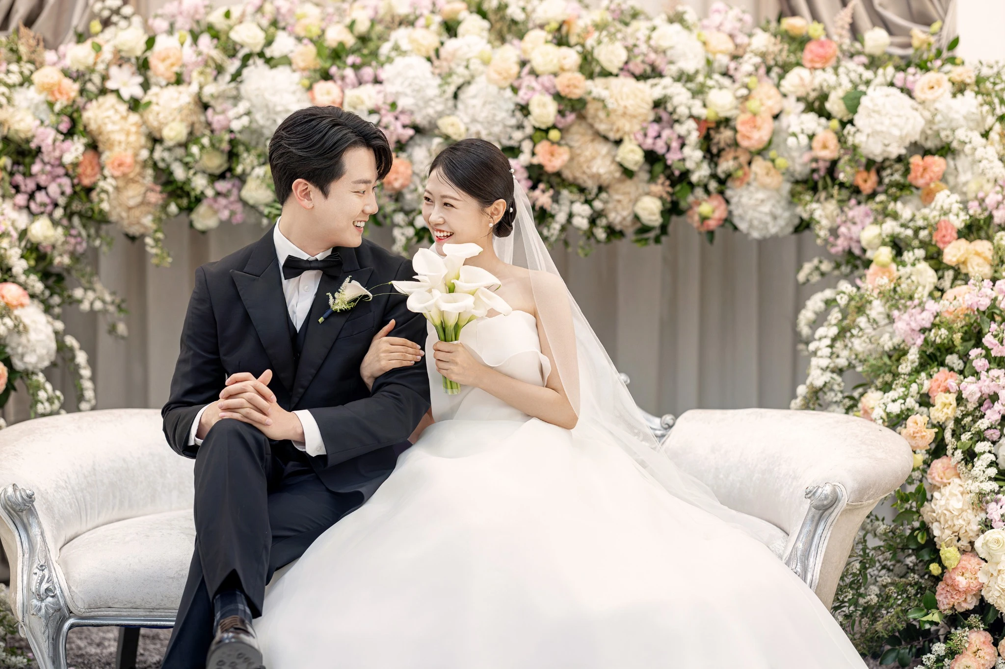 어두운 홀 플라워 커플 컷으로, 대형 플라워 아치가 있는 어두운 홀와 샹들리에과 플라워아치가 함께 보이는 장면입니다.