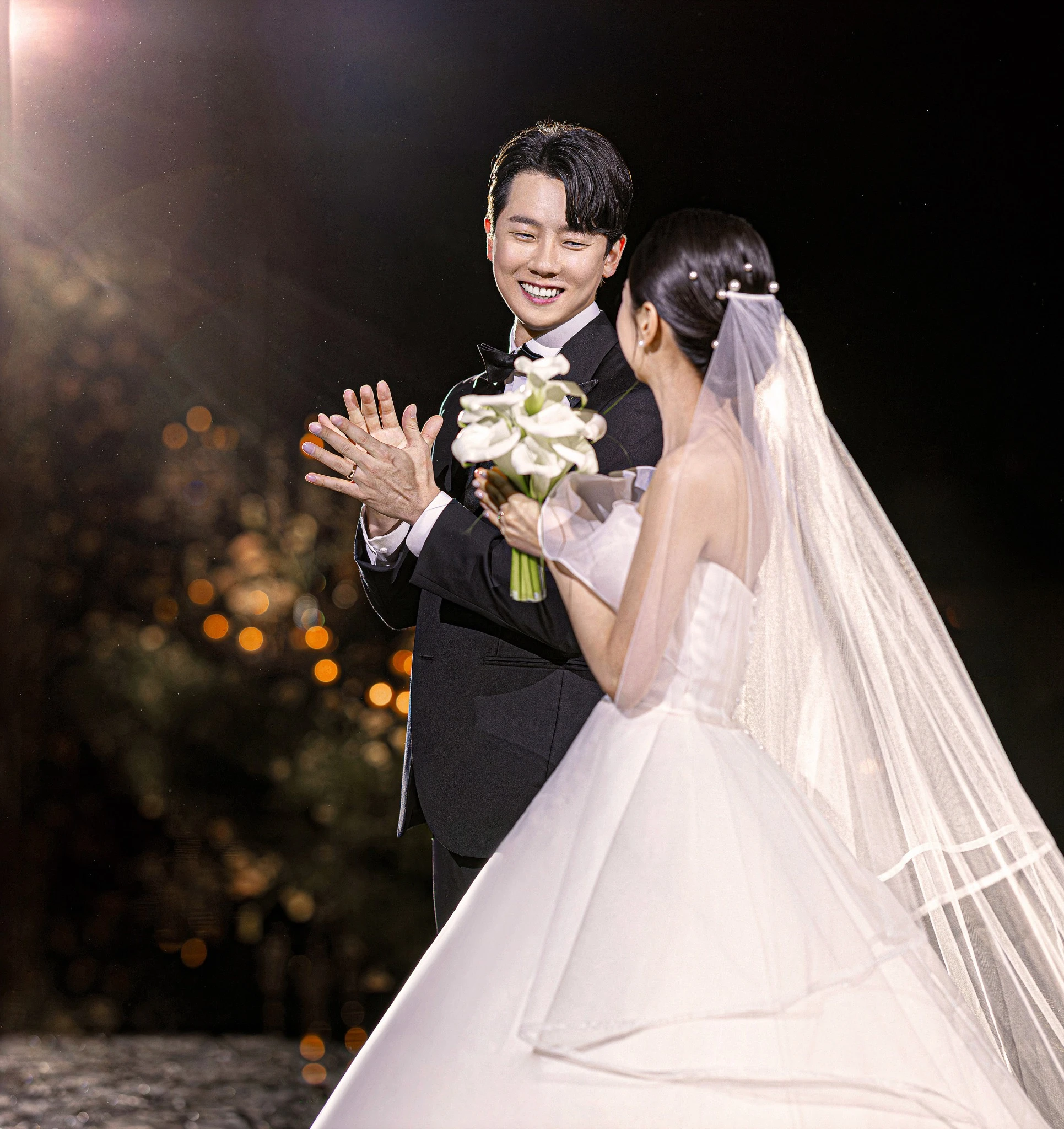 신부 클로즈업 컷으로, 어두운 홀과 흐린 촛불 배경와 베일와 부케 일부가 함께 보이는 장면입니다.