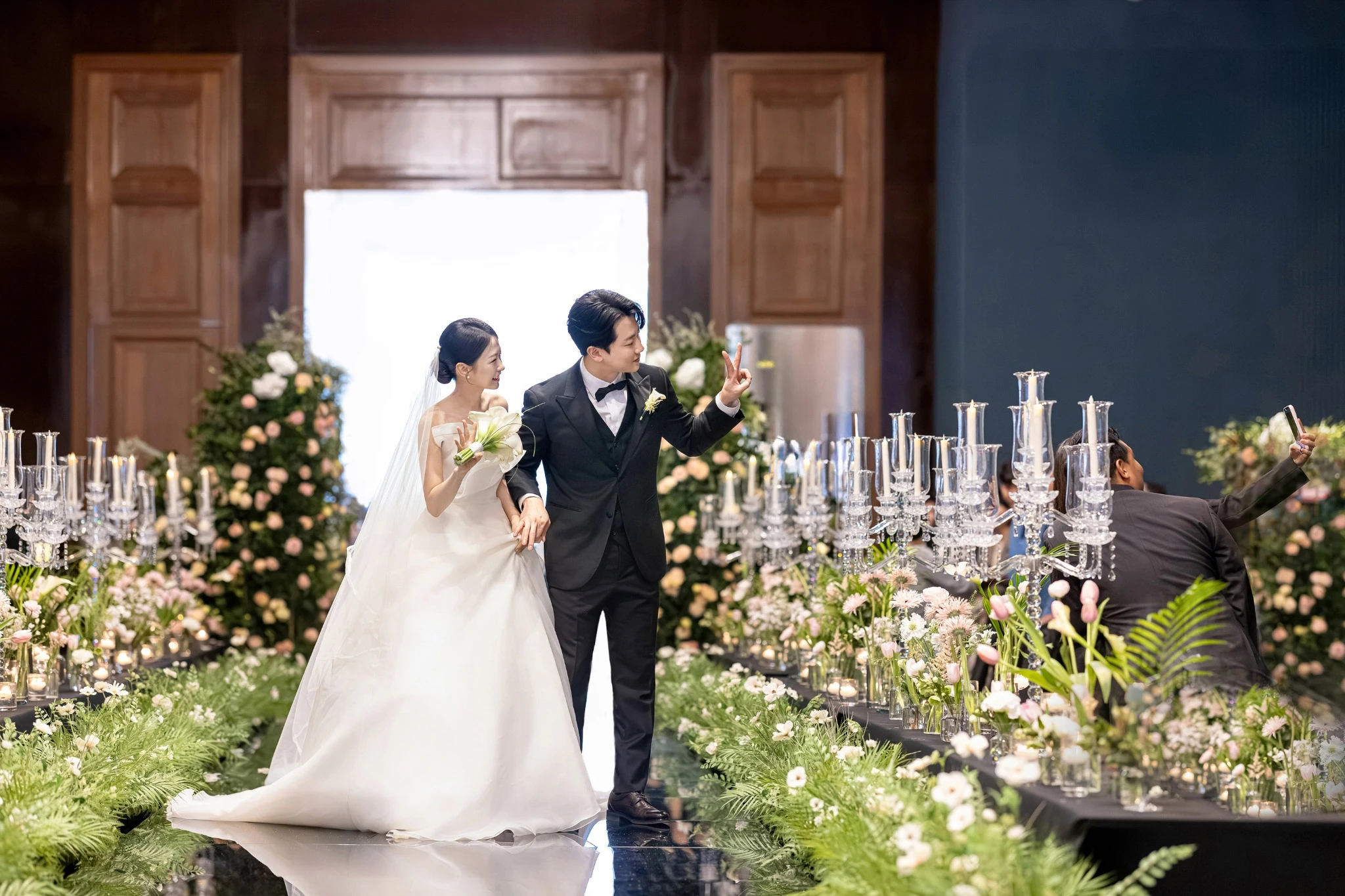 커플 리액션 컷으로, 어두운 홀의 스포트라이트 주변와 부케과 베일가 함께 보이는 장면입니다.