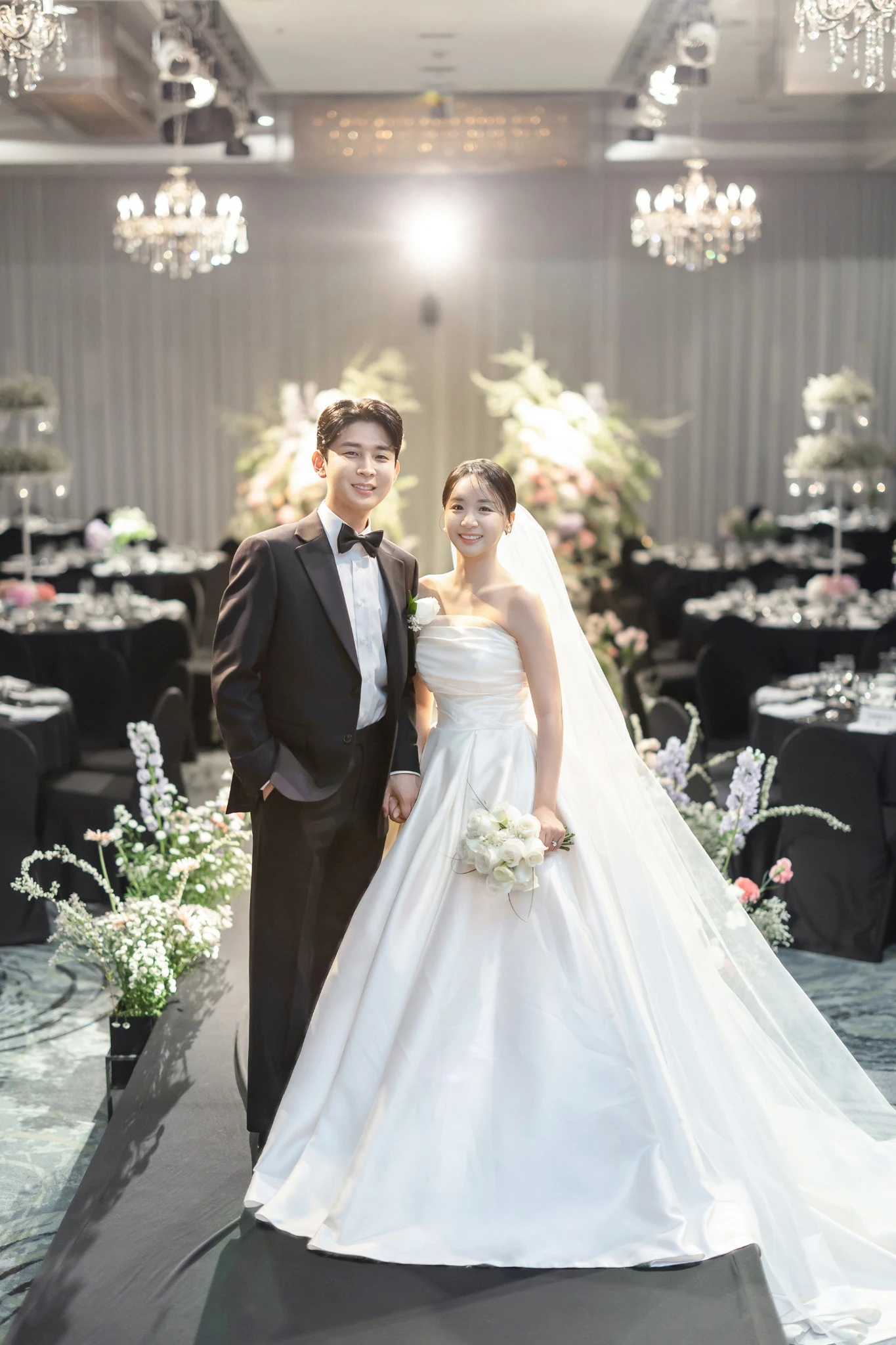 문 프레임 입장 장면으로, 꽃 장식이 놓인 열린 문 입구와 대형 문와 꽃기둥가 함께 보이는 장면입니다.