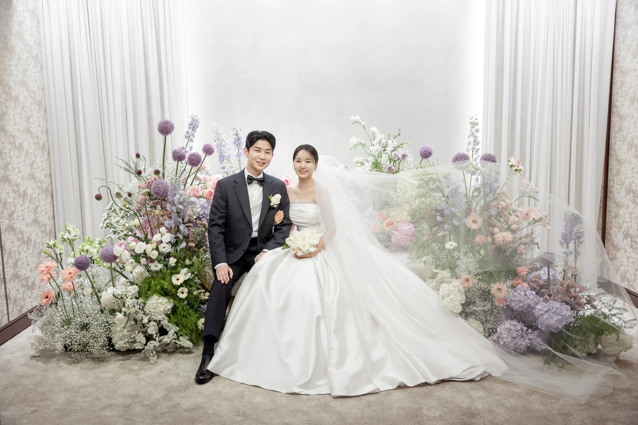 신랑 후면 시선 컷으로, 어두운 하객석 배경의 버진로드 주변와 베일와 부케가 함께 보이는 장면입니다.