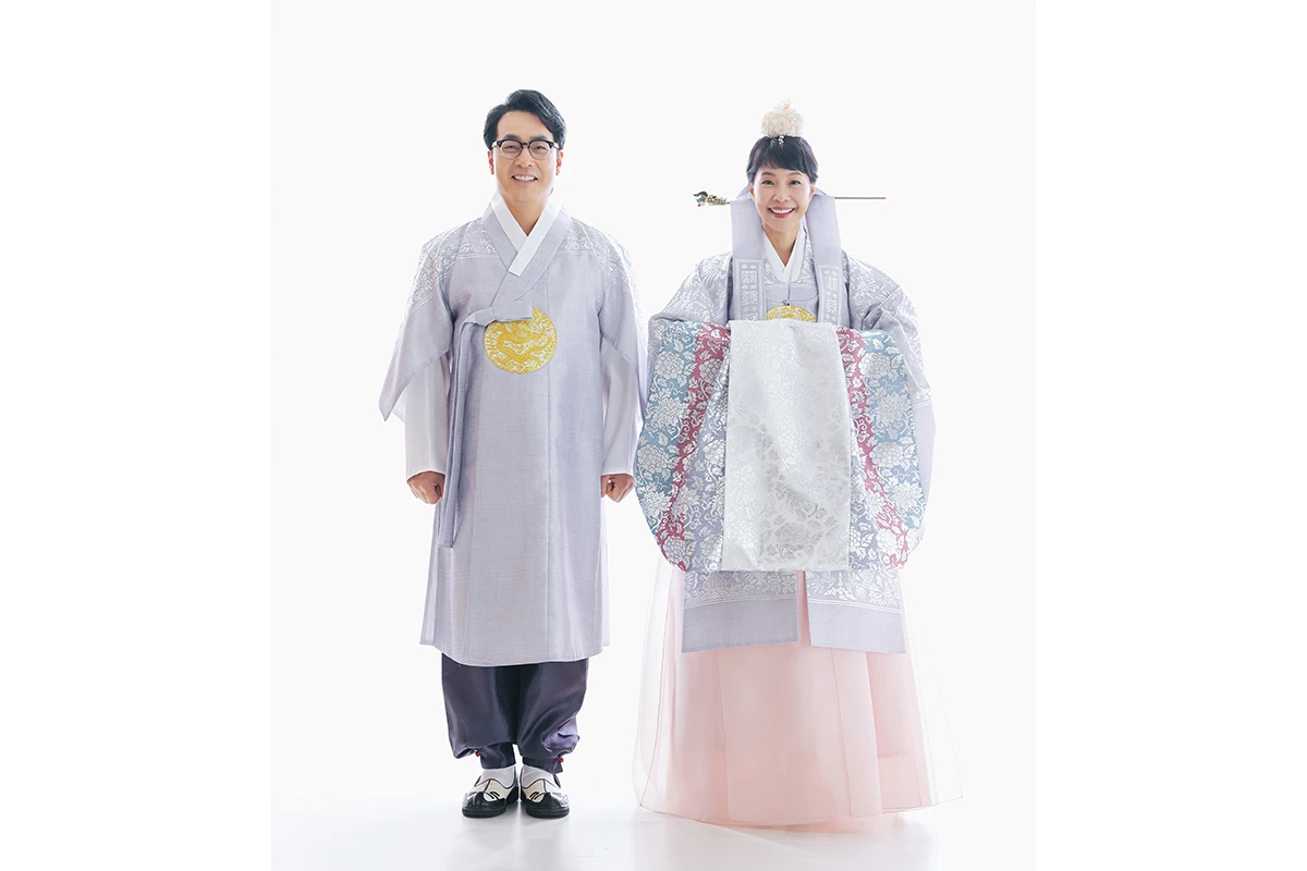 매우 밝은 흰색 스튜디오에서 한복을 입은 성인 2명이 흰 배경 앞에 나란히 선 전신 사진이며, 흰 배경과 바닥가 장면의 구성을 보완합니다.