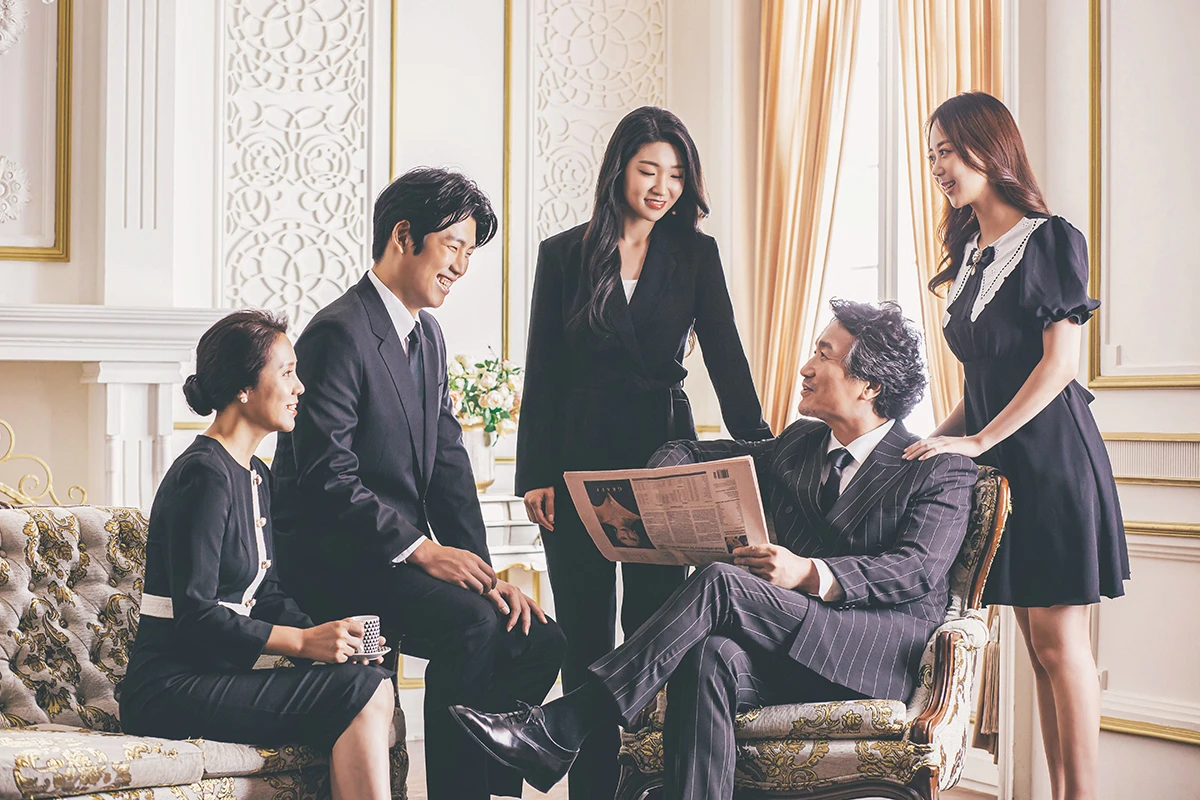 흰 벽돌과 큰 창이 있는 밝은 실내에서 검정과 흰색 의상의 성인 3명과 아동 1명, 반려견 1마리가 흰 벽돌 배경 앞에 있는 사진이며, 의자, 흰 반려견가 장면의 구성을 보완...