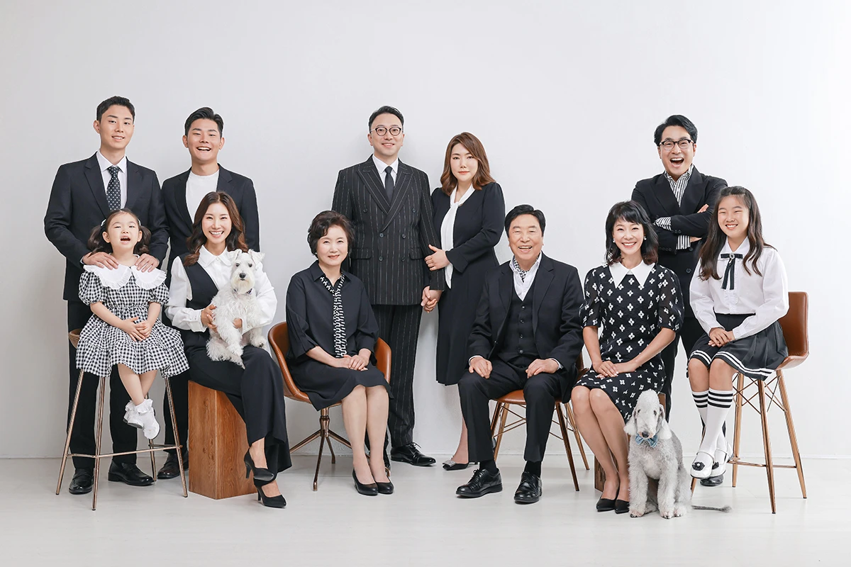 샹들리에와 소파가 있는 클래식 실내에서 검정 정장을 입은 성인 5명이 클래식 소파 주변에서 대화하듯 배치된 사진이며, 신문, 소파, 찻잔가 장면의 구성을 보완합니다.