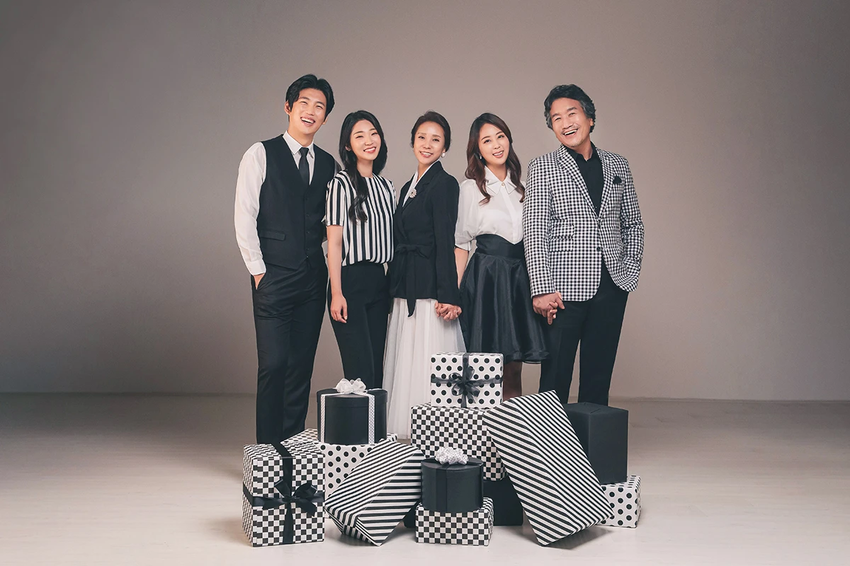 회색 스튜디오 배경에서 검정과 흰색 의상의 여성 3명이 회색 배경 앞에 앉고 선 사진이며, 의자와 상반신 중심 배치가 장면의 구성을 보완합니다.