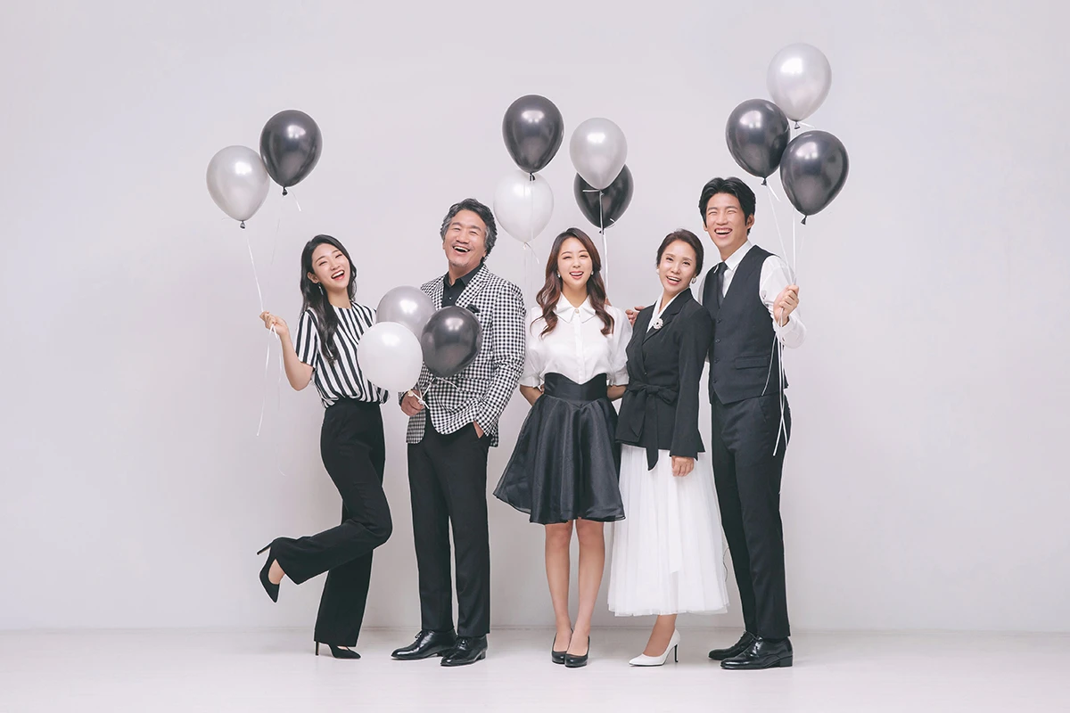 회색 스튜디오 배경의 흑백 사진에서 남성 2명이 흑백 톤으로 우산과 의자를 활용해 촬영된 분할 구성 사진이며, 우산, 의자, 러그가 장면의 구성을 보완합니다.