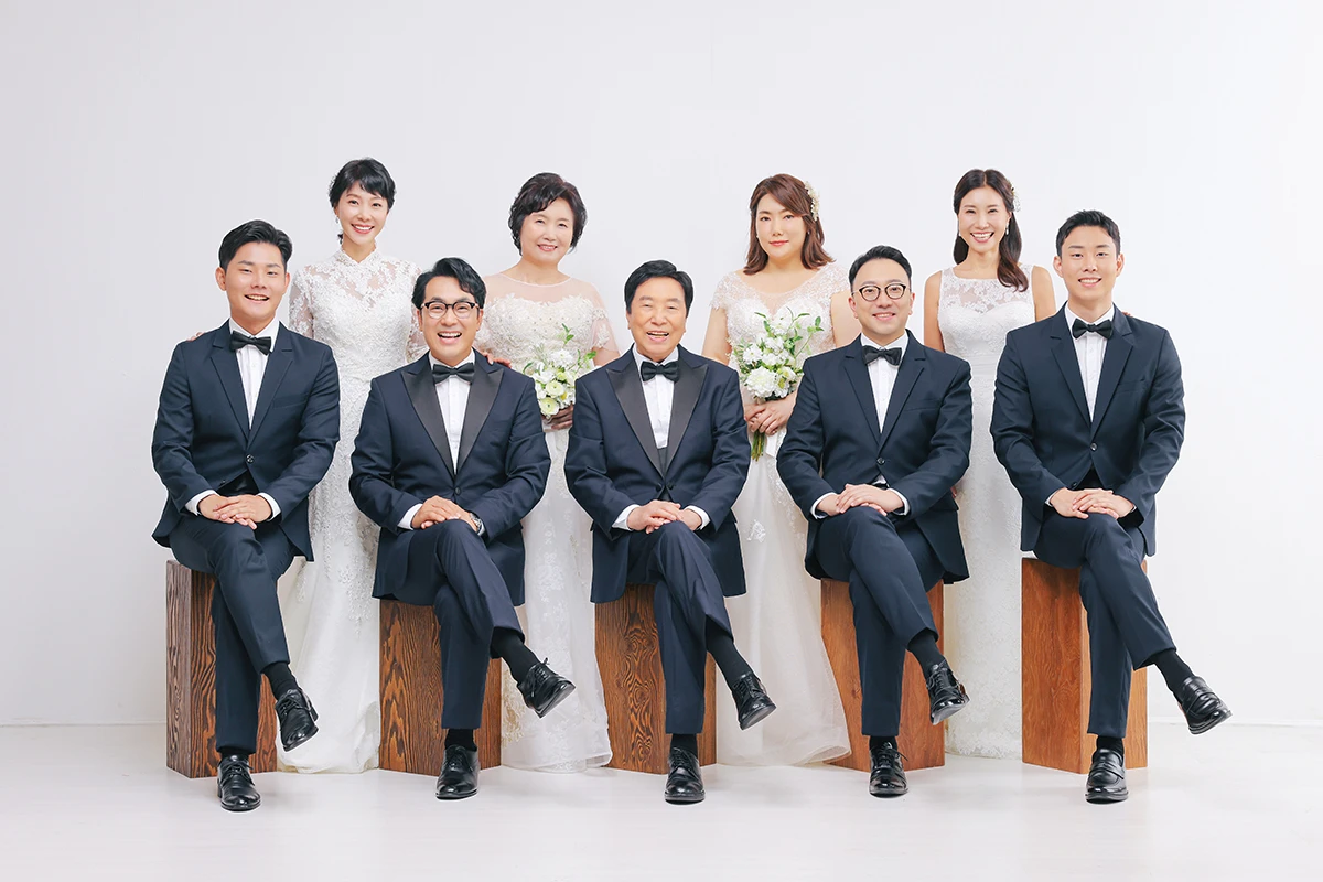 밝은 창가와 꽃 장식 실내에서 화이트 드레스와 베일을 착용한 성인 1명이 꽃 장식 사이에 앉은 사진이며, 분홍색 꽃 장식과 베일가 장면의 구성을 보완합니다.
