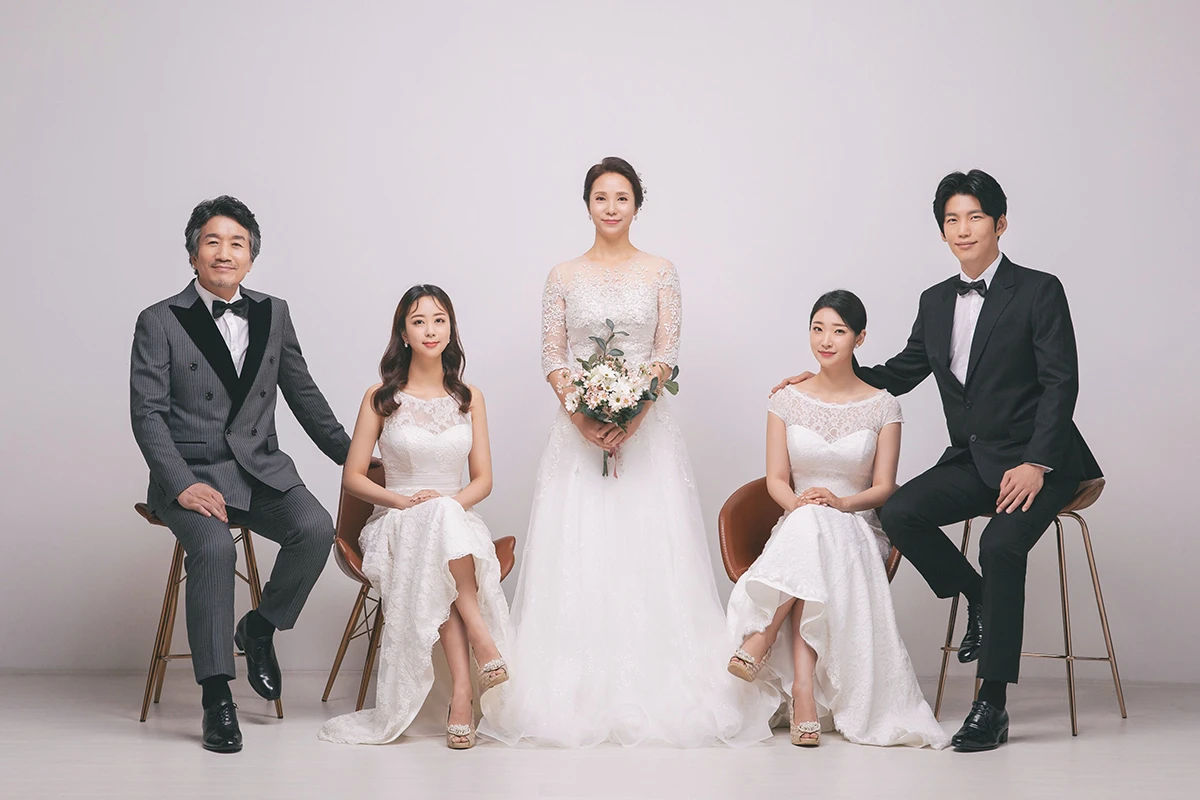 흰 셔터와 꽃 장식이 있는 실내에서 베이지와 화이트 의상을 입은 성인 5명이 꽃과 셔터 장식 앞에 선 사진이며, 꽃바구니와 셔터 장식가 장면의 구성을 보완합니다.