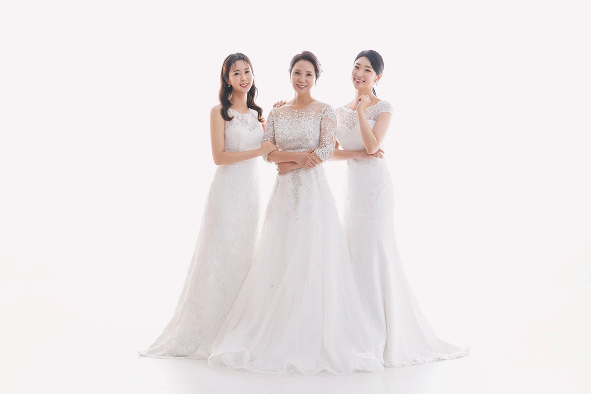 갈색 단색 배경의 스튜디오에서 베이지와 화이트 의상의 성인 5명이 갈색 배경 앞 의자와 스툴 주변에 배치된 사진이며, 나무 의자와 스툴가 장면의 구성을 보완합니다.