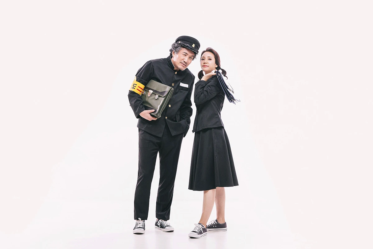 밝은 흰색 스튜디오에서 흰 셔츠와 청바지를 입은 성인 4명이 흰 배경 앞에서 바닥에 누워 포즈를 만든 사진이며, 청바지와 흰 운동화가 장면의 구성을 보완합니다.