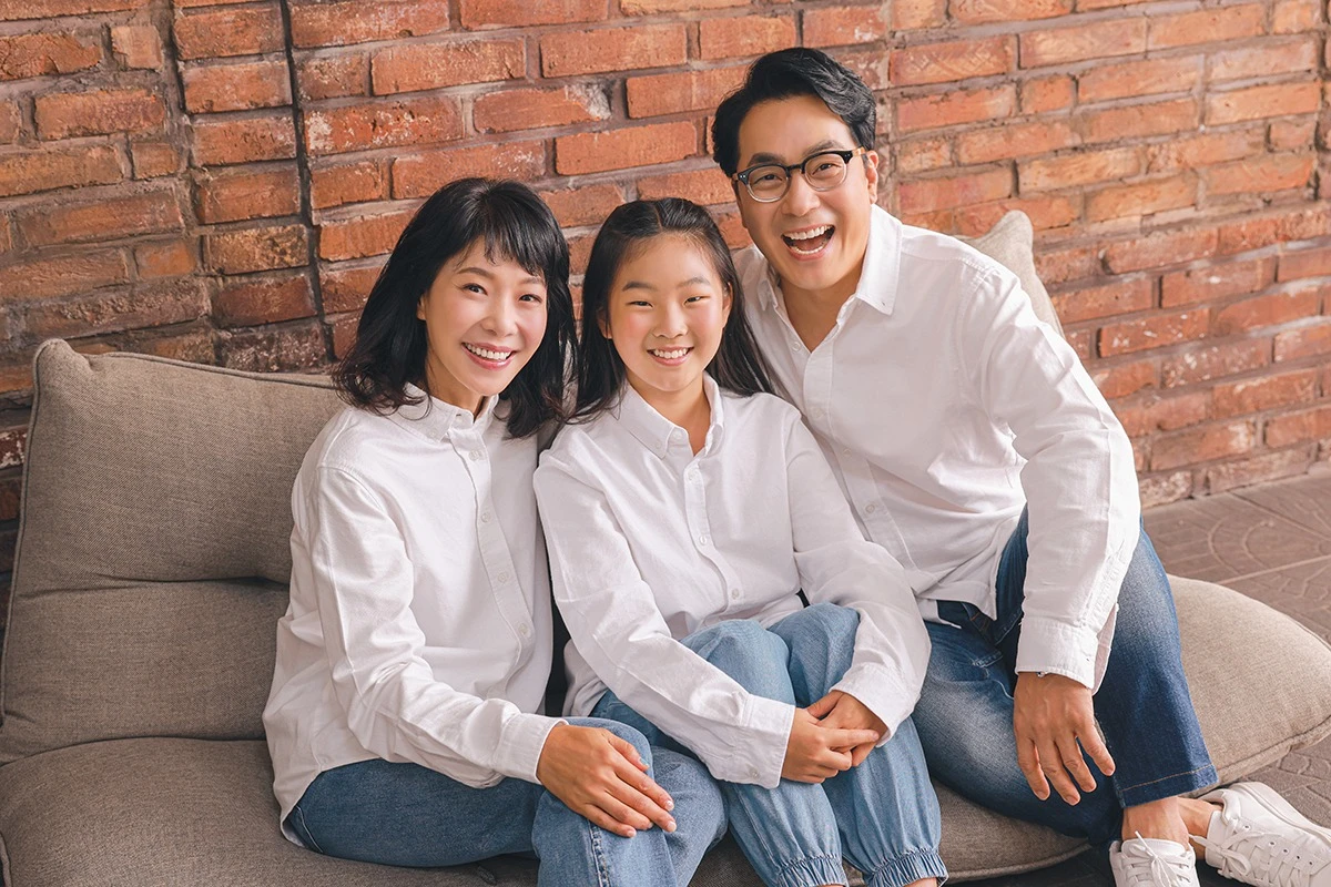 밝은 흰색 스튜디오에서 흰 셔츠와 청바지를 입은 성인 4명이 흰 배경 앞에서 서로를 업은 사진이며, 청바지와 흰 셔츠가 장면의 구성을 보완합니다.